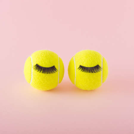 Two tennis balls with lashes on a pink background. Sports tennis competition surreal conceptの写真素材