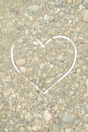 Sand with stones in which a white heart shaped frame is placed. Summer concept of beach and loveの写真素材