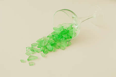 A glass for drinking from which neon green pebbles come out on a cream background. Summer party conceptの写真素材