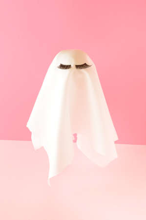 White ghost costume with lashes on a pink background. Romantic Halloween minimal composition.の写真素材