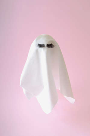 White ghost with lashes on a pink background. Halloween scary background. Minimal compositionの写真素材