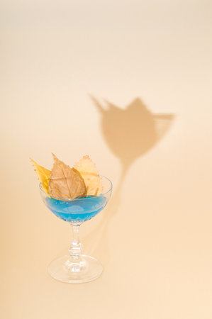 Autumn blue cocktail decorated with dry fallen leaves with an unusual shade. Cream wallpaper. Autumn concept for parties and celebrationsの写真素材