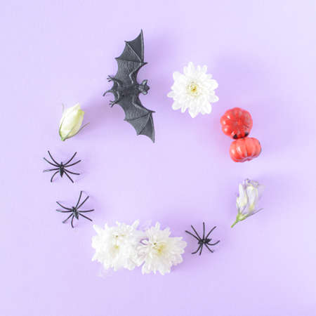 Round frame made of Halloween items, bat, spiders, flowers, and pumpkins on a purple background.の写真素材