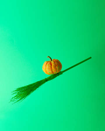 Pumpkin painted in several colors flying on a witch broom. Illuminated by green light. Halloween minimal futuristic concept.の写真素材
