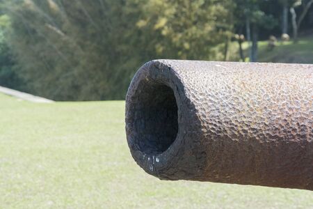 Front view of a rusty old cannon. Cannon for war against boats at fort in island of Florianopolis - Brazil. Cannon on grass and rocks background.の写真素材
