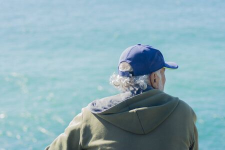 White-haired man in cap looking out to sea from the cliff top.の写真素材