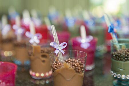 Closeup of transparent cups with chocolate and plastic spoon with blue bow on children's party. Selective focus.の写真素材