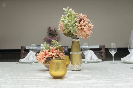 Decorative flowers in beautiful vases on a dining table next to a candle. Simple decoration of wedding anniversary. Text area. Copy space Selective focus.の写真素材