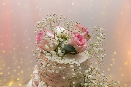 Close up of beautiful white tree tier cake with fresh flowers with fairly light and lanterns glowing...