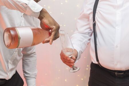 Man pouring champagne rose into crystal glass held by a gentleman wearing white shirt and suspender....