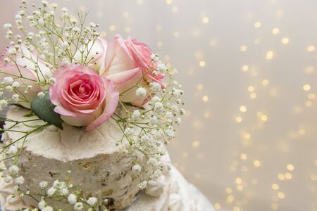 Close up of beautiful white tree tier cake with fresh flowers with fairly light and lanterns glowing in the background on a wooden rustic table. Selective focus. Copy space.の写真素材
