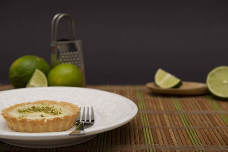 Side view of lemon tart on dish plate with lemon slices on table. Lemon tartlet with zest on top. Strawberry Pastry. Sweet with citrus fruit. Selective focus. Copy space.の写真素材