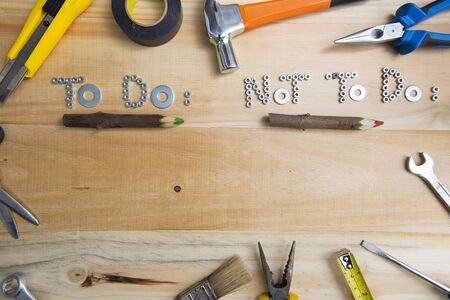 Top view of the phrases "to do" and "not to do" made of nuts and washers on a wooden surface underlined by rustic wooden pencils. Construction tools framing wooden background shot from above.の写真素材