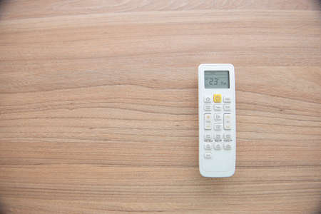 A flat lay of the remote control of an air conditioner on a wooden surface. Display showing temperature of 23Âº Celsius. Concept of temperature control and global warming. Copy space.の写真素材