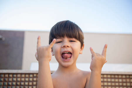 Portrait of a boy sticking out his tongue and making the rock and roll symbol with both hands. Boy without a shirt and with a rocker attitude.の写真素材