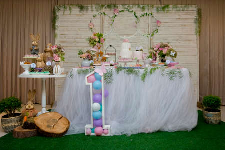 Luxurious table of sweets and birthday cake decorated with flower arrangements and delicate wild...