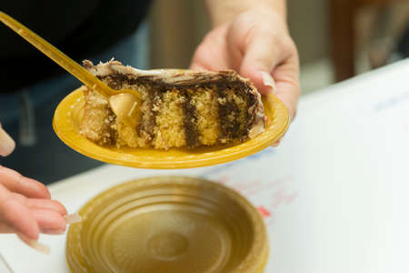 Female hands holding yellow disposable plastic dish with home made cake. Piece of cake filled with...