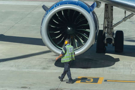 worker with earmuffs and uniform walking in front of airplane turbineのeditorial素材