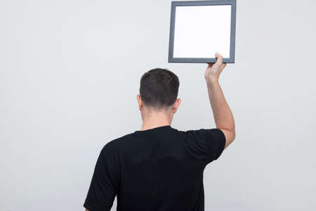 Back view of man holding blank board with black frame over head on white background. Copy space....