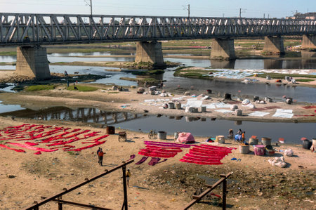 Agra, India. January 27, 2017. The Indians wash clothes in a dirty river under a bridge and drying clothes on the sand.のeditorial素材