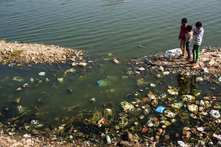 Environmental issues in India. Children playing near dirty littered with debris of the lake, watching the fish. Near the water Palace in Jaipur India. Photo taken 23 February 2017.のeditorial素材