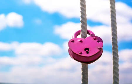 Pink Wedding closed lock in the form of heart. The castle weighs in at a bridge on a blue sky background on a bright Sunny day.の写真素材