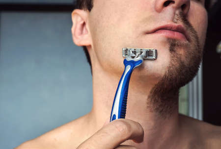 Health beauty and skin care concept. Handsome young man with half shaved and half bearded face on grey blue backgroundの写真素材