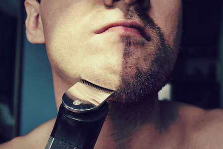 a man mowing a beard with hair clippers hair. Half face with a beard half shaved.