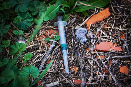 A used syringe was lying on the ground. The addict threw the syringe in the grassの写真素材