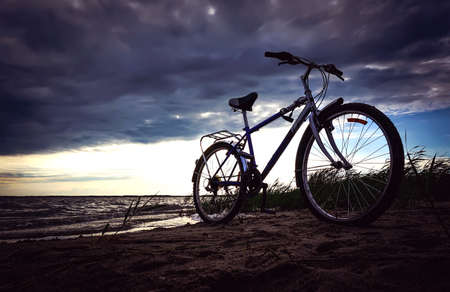 The blue bike is on the beach at the lake at the beautiful sunset. Romantic bike ride in nature.の写真素材