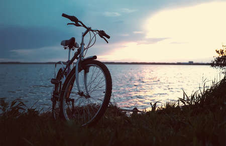 The blue bike is on the beach at the lake at the beautiful sunset. Romantic bike ride in nature. Toned retro photo.の写真素材