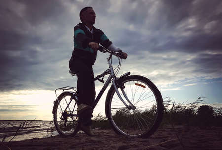 A man rides his mountain bike on a beach. The guy riding on the beach by bike near the lakeの写真素材