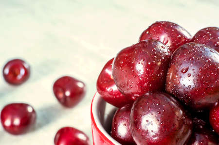 Ripe sweet cherries in a red cup on white wooden background, tasty and healthy dessertの写真素材