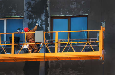 The gondola lift or scaffold with the worker on the building construction site. workers plastered the wall of the buildingの写真素材