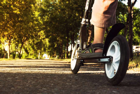 Child's feet in sandals standing on the scooter. black scooter wheels. at scooter's