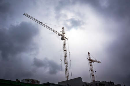 two high tower crane and building under construction against the dark sky.の写真素材