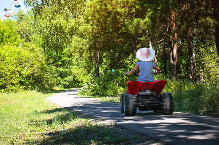 Baby girl riding on a red ATV in a green Park under the rays of the bright sunの写真素材