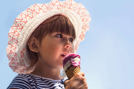 Small European kid holding a ice cream and looking into the distance. on blue isolated backgroundの写真素材