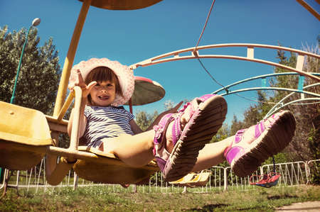 Little girl child sitting on a revolving carousel in the Park. Happy and joyful expression. tinted photoの写真素材