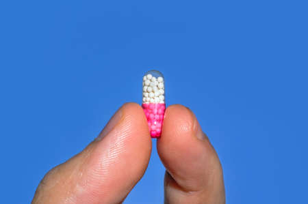Hand holding capsule pill on blue isolated backgroundの写真素材