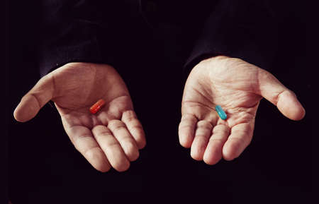 Red tablet in the left palm blue pill in his right handの写真素材