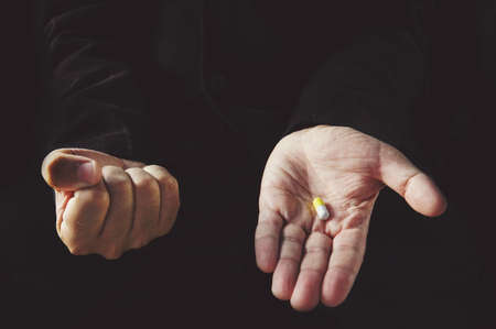 Tablet in hand. Male hand holding pill. Choosing the right treatmentの写真素材