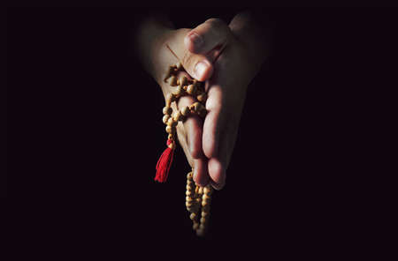 Hands folded in prayer on a black isolated background. The priest in prayer. Rosary in the hands of menの写真素材