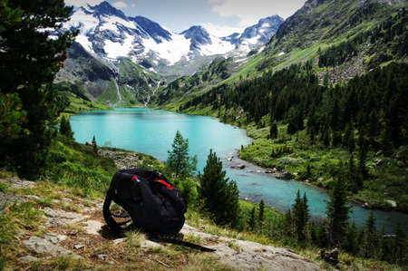 Black Backpack lying on the stone against a mountain landscape with turquoise lake. The concept of Hiking in the wild.の写真素材