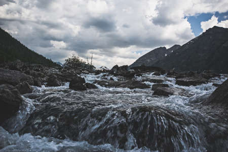 Dark gloom mountain valley along the mountain river on the background of snow peaks and ice glacier, Altai mountains, Siberia, Russiaの写真素材