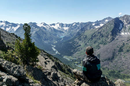Lonely man looking at a river valley sitting on a rock. Green mountains in the distance. Sunny day....