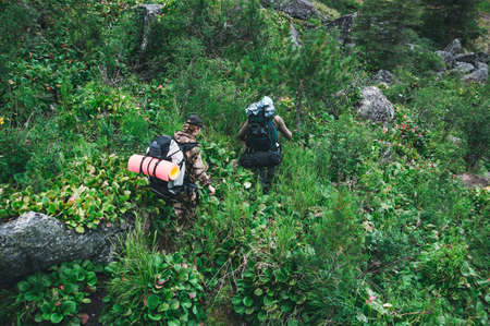 adventure, travel, tourism, hike and people concept - close up of friends walking with backpacks in woods from back. A guy and a girl with large heavy backpacks go through the forestの写真素材