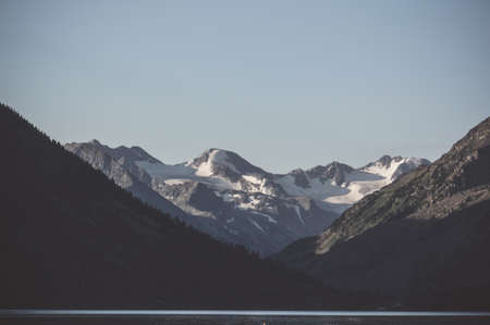 Gloomy landscape with lake and Snow caps the high mountains in the background in evening light. Dark...