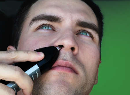 Portrait of handsome man using a hair trimmer for nose, on a green background, close up