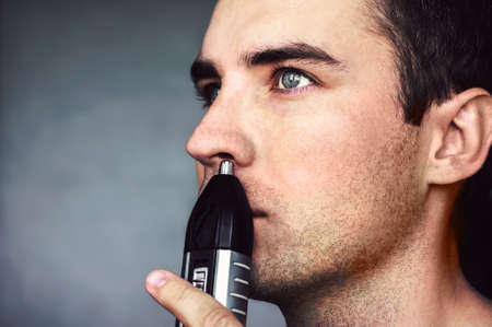 A young man removes hair from the nose electric trimmer. on a dark background.の写真素材